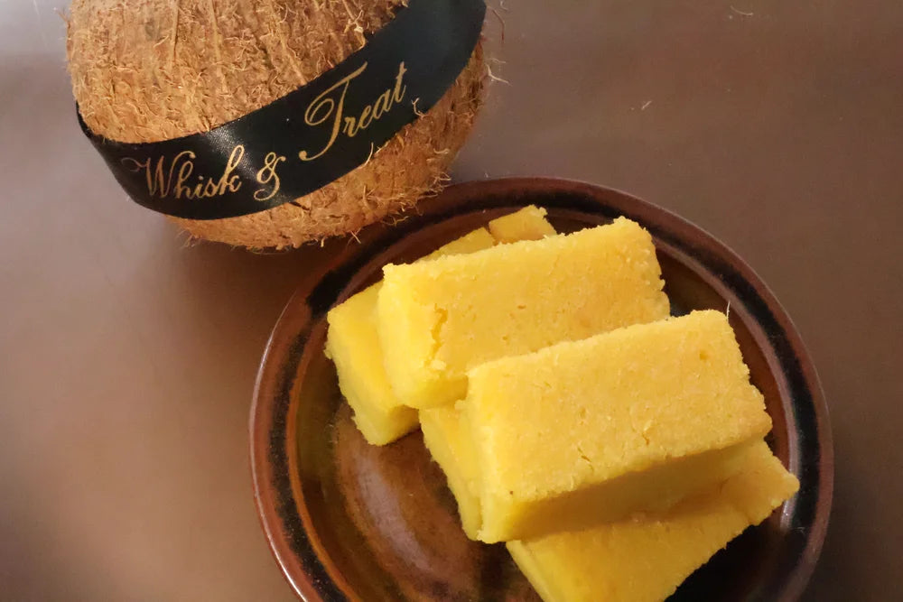Yellow soap bars in a brown dish with a coconut labeled 'Whisk & Treat' on a brown background
