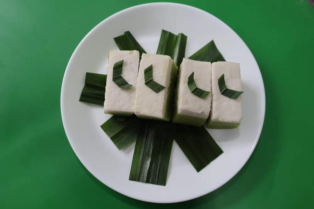Four pieces of tofu arranged on a bed of green leaves on a white plate with a green background