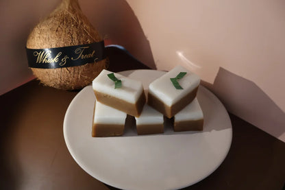 Coconut and white bar of soap with green leaves on a white plate against a beige background
