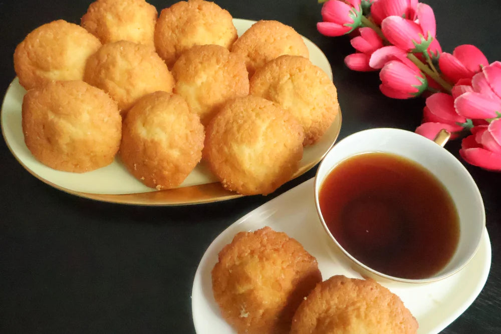 Fried dough balls on a plate with a side of tea on a dark surface.