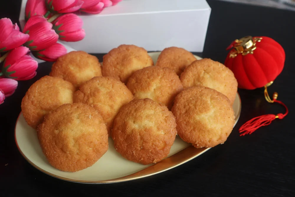 Plate of fried dough balls on a dark surface with pink flowers and a decorative item in the background.